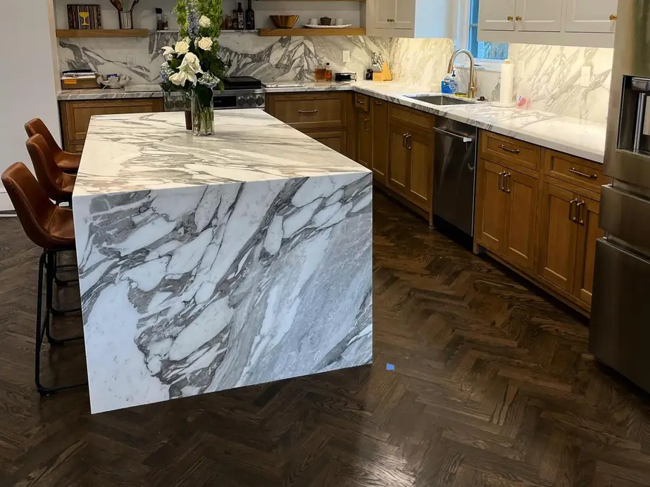 White marble kitchen island with a waterfall end, a matching slab backsplash and an undermount sink on the back run