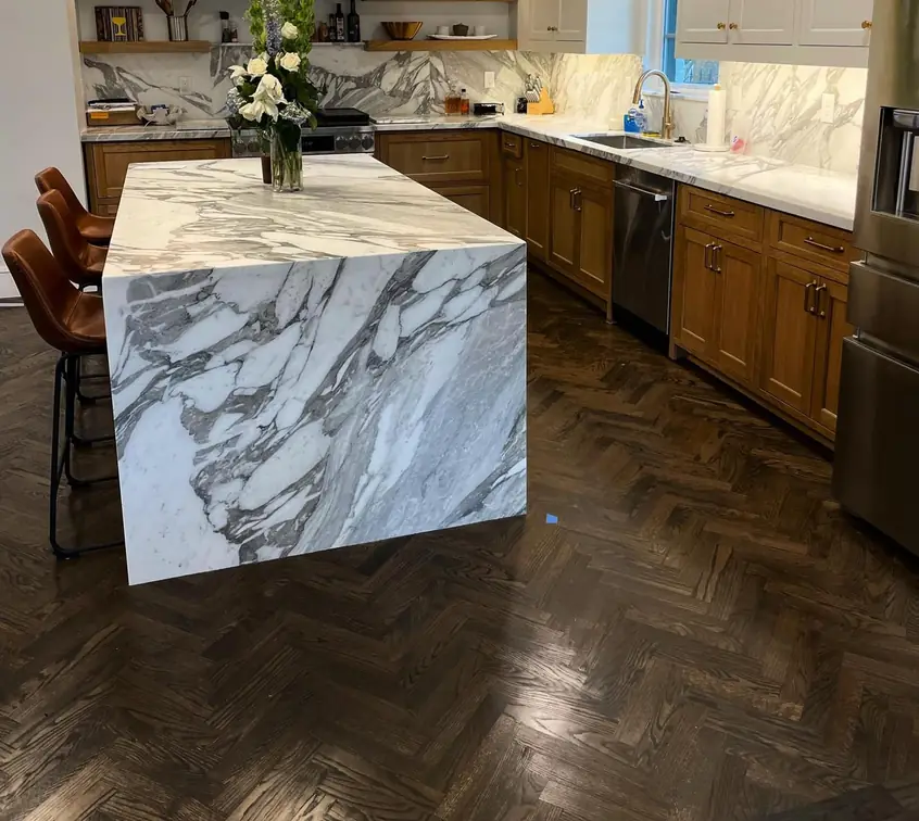 White marble kitchen island with a waterfall end and a matching marble slab backsplash behind the range