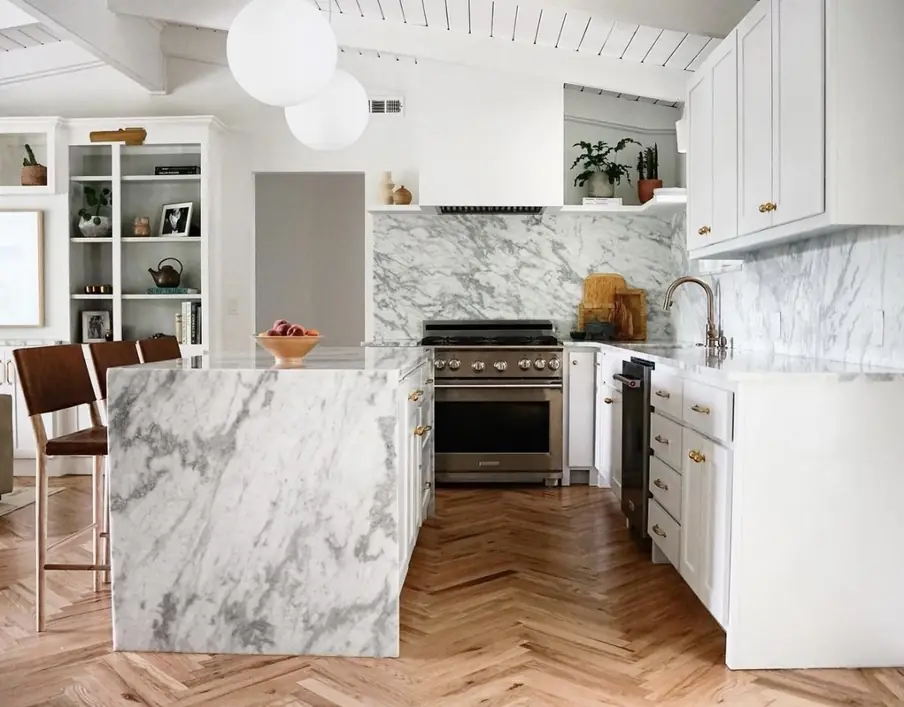 A white marble waterfall island and slab backsplash in a white kitchen
