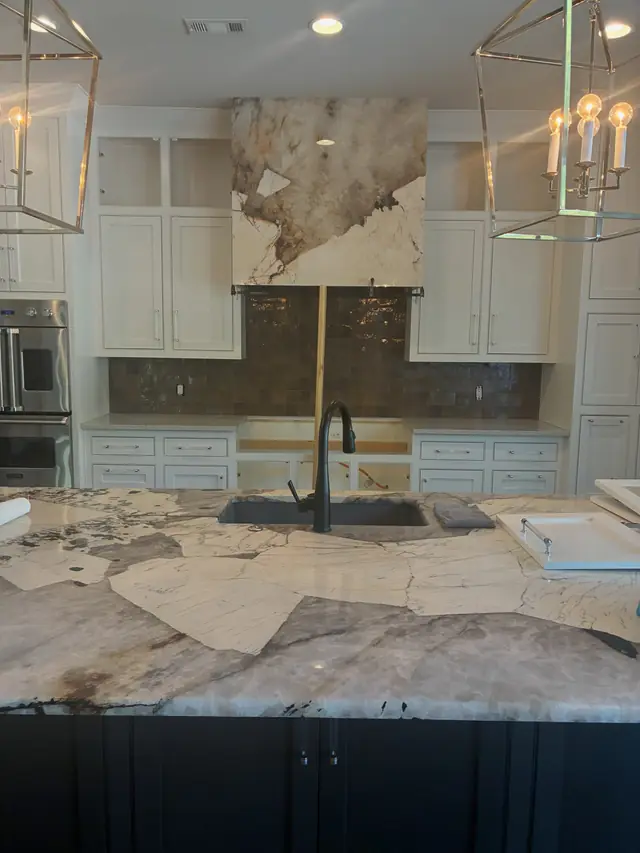 A white and grey quartzite island with a matching stone range hood surround, still unfinished