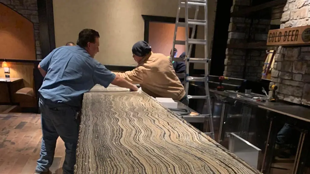 Two installers setting a long striped stone bar top in a restaurant